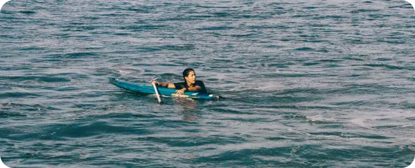 Josselyn Alabi paddling out on her board in the ocean in El Salvador